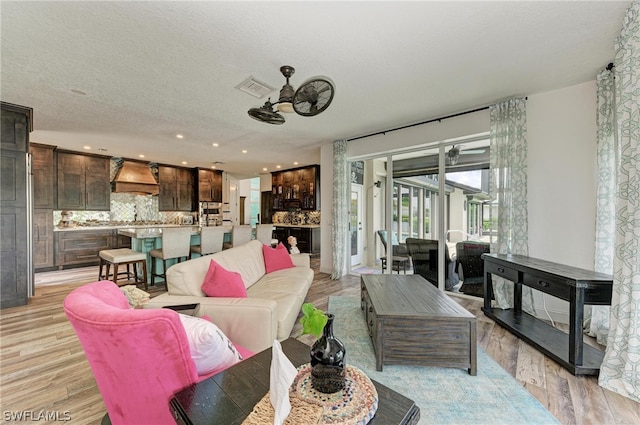 living room featuring light wood-type flooring, a textured ceiling, and ceiling fan