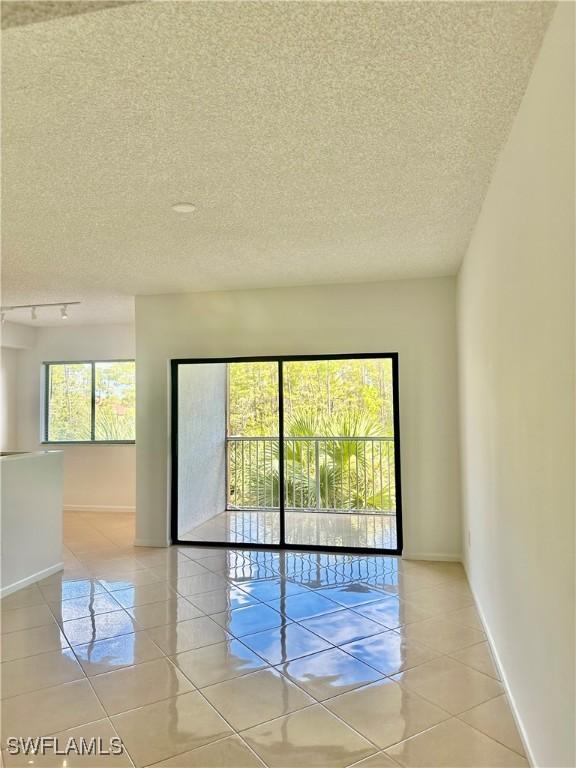 unfurnished room with track lighting, light tile patterned floors, baseboards, and a textured ceiling