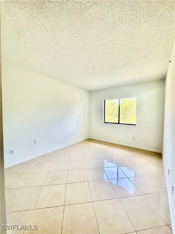 spare room featuring light tile patterned floors, baseboards, and a textured ceiling