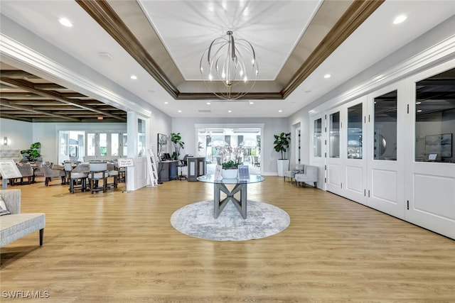 foyer entrance featuring a raised ceiling, light hardwood / wood-style flooring, a chandelier, and ornamental molding