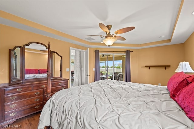 bedroom with ceiling fan, access to exterior, wood-type flooring, and a tray ceiling