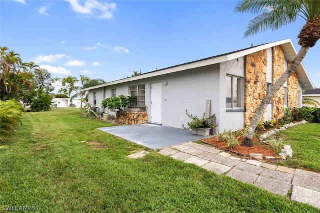 view of front of home with a front yard, stone siding, a patio area, and stucco siding