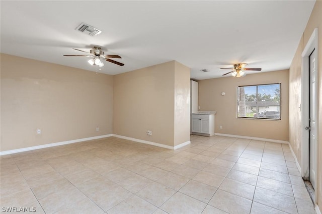 empty room featuring ceiling fan, light tile patterned flooring, visible vents, and baseboards