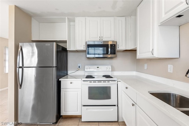 kitchen featuring light tile patterned floors, a sink, white cabinetry, appliances with stainless steel finishes, and light stone countertops