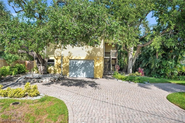 view of front of home featuring stairs, a garage, fence, and decorative driveway