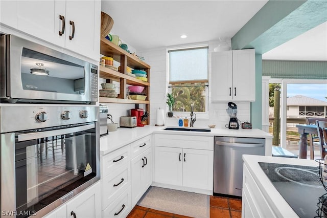 kitchen with sink, decorative backsplash, white cabinets, dark tile patterned flooring, and appliances with stainless steel finishes