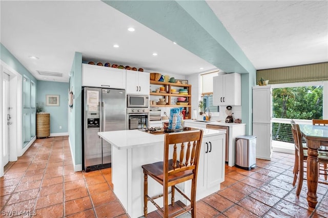 kitchen with stainless steel appliances, open shelves, white cabinetry, light countertops, and a kitchen island