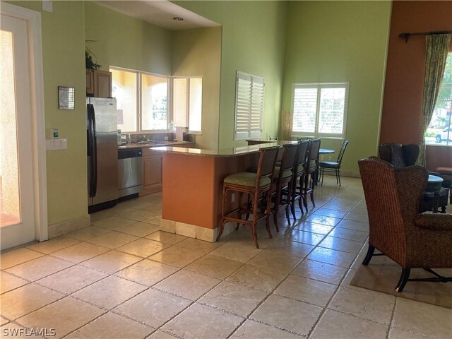 kitchen featuring baseboards, stainless steel appliances, a high ceiling, and a kitchen breakfast bar