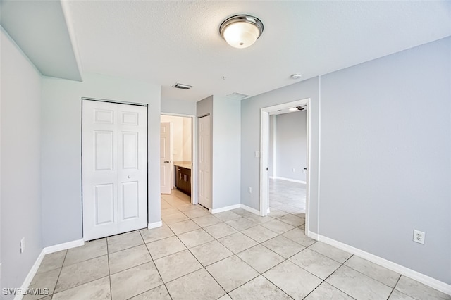 unfurnished bedroom with a textured ceiling, light tile patterned flooring, visible vents, and baseboards