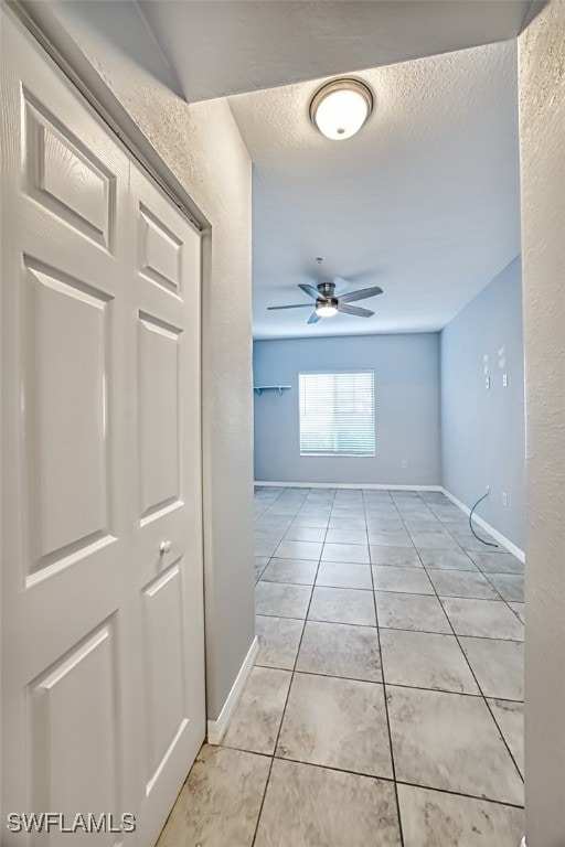 hallway with a textured ceiling, a textured wall, light tile patterned floors, and baseboards