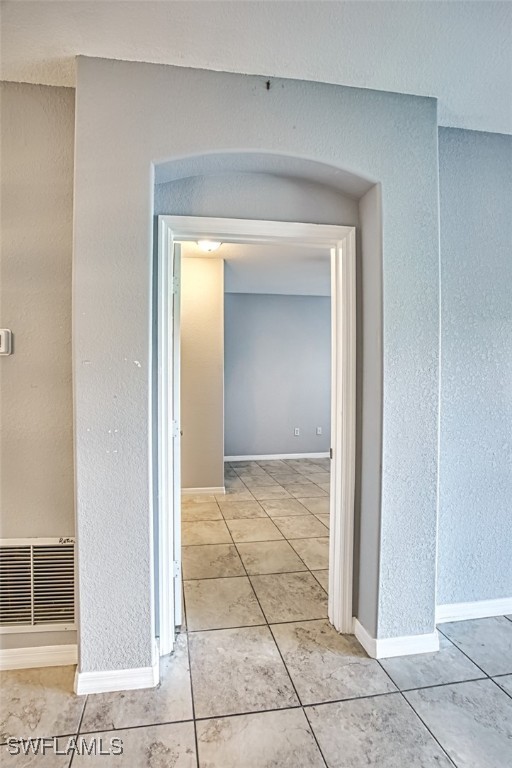 hallway featuring light tile patterned floors, arched walkways, visible vents, and baseboards