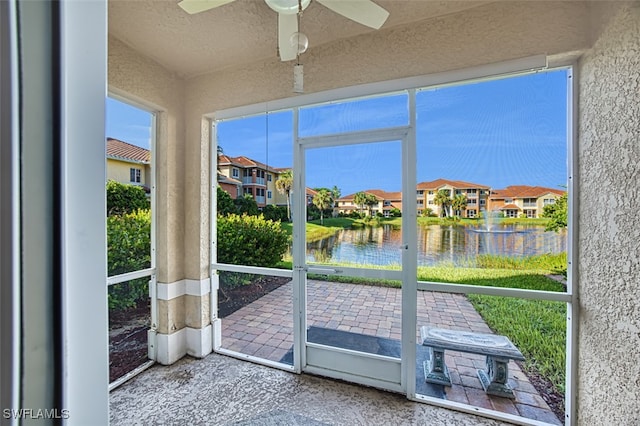 unfurnished sunroom featuring ceiling fan, a water view, and a residential view