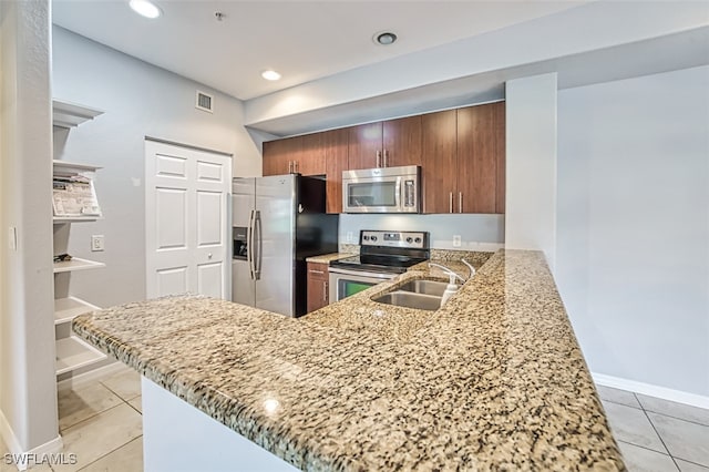 kitchen featuring a peninsula, appliances with stainless steel finishes, a sink, and light stone countertops