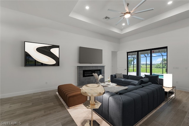 living room with a high ceiling, a raised ceiling, ceiling fan, hardwood / wood-style floors, and a tiled fireplace