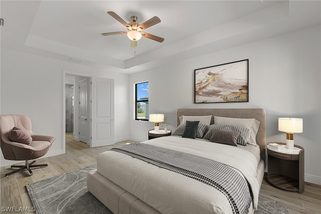 bedroom featuring a raised ceiling, light hardwood / wood-style flooring, and ceiling fan