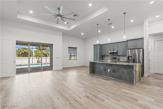 kitchen featuring ceiling fan, hanging light fixtures, light stone counters, a kitchen island with sink, and appliances with stainless steel finishes