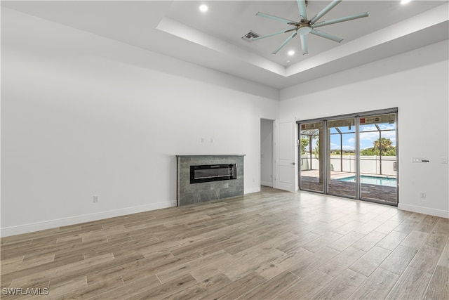 unfurnished living room featuring a tiled fireplace, ceiling fan, light hardwood / wood-style flooring, and a towering ceiling