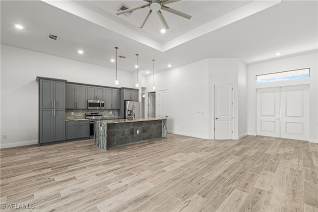 kitchen featuring appliances with stainless steel finishes, light wood-type flooring, gray cabinetry, hanging light fixtures, and an island with sink