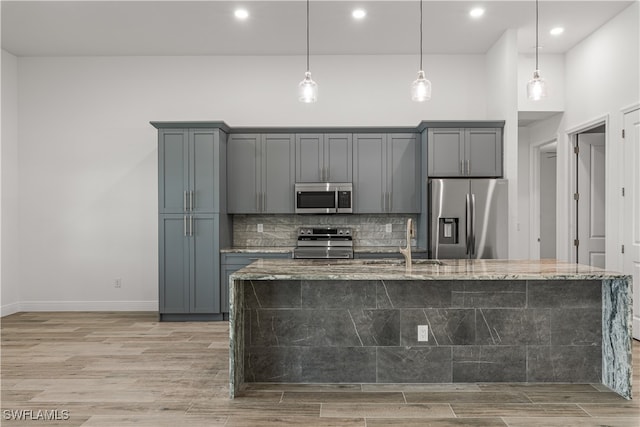 kitchen featuring light stone countertops, appliances with stainless steel finishes, light wood-type flooring, and hanging light fixtures