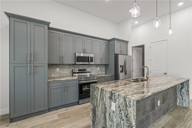 kitchen with gray cabinetry, light hardwood / wood-style floors, light stone counters, and appliances with stainless steel finishes