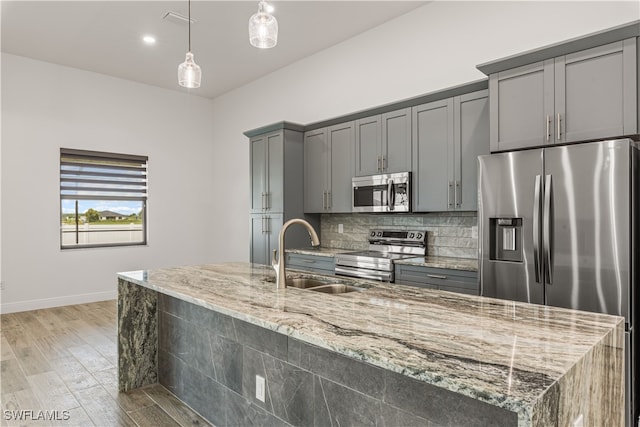 kitchen with pendant lighting, sink, light wood-type flooring, appliances with stainless steel finishes, and light stone counters