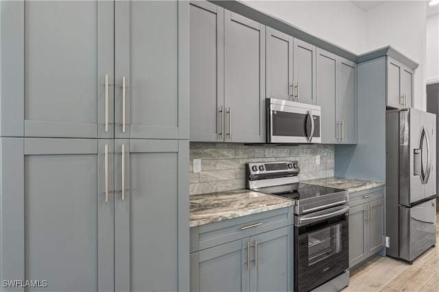 kitchen featuring gray cabinetry, light wood-type flooring, light stone countertops, and stainless steel appliances