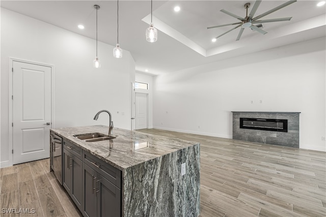 kitchen with a kitchen island with sink, sink, dark stone countertops, decorative light fixtures, and dark brown cabinets