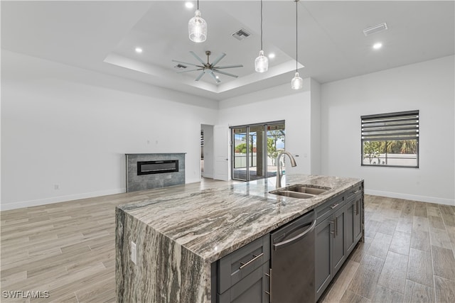 kitchen featuring light stone counters, stainless steel dishwasher, sink, light hardwood / wood-style floors, and an island with sink