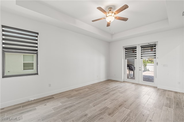 empty room featuring french doors, light wood-type flooring, a raised ceiling, and ceiling fan