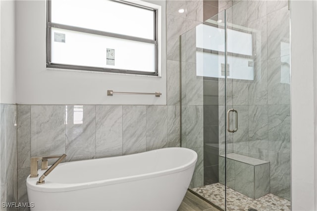 bathroom with separate shower and tub, a healthy amount of sunlight, and tile walls