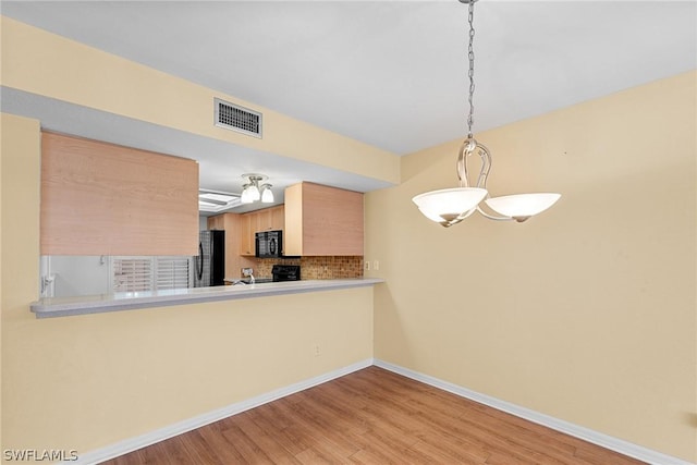 kitchen with visible vents, light brown cabinets, light wood-type flooring, a peninsula, and black appliances