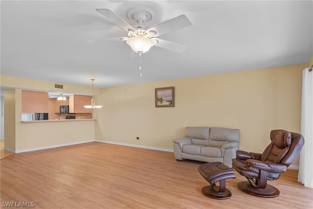 living room featuring visible vents, light wood-style flooring, baseboards, and ceiling fan with notable chandelier