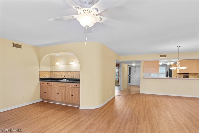 unfurnished living room with visible vents, ceiling fan, a sink, and light wood finished floors