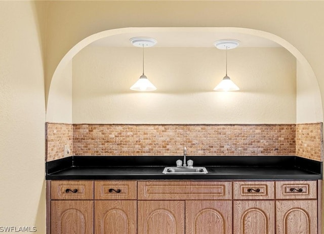 kitchen featuring tasteful backsplash, dark countertops, a sink, and hanging light fixtures