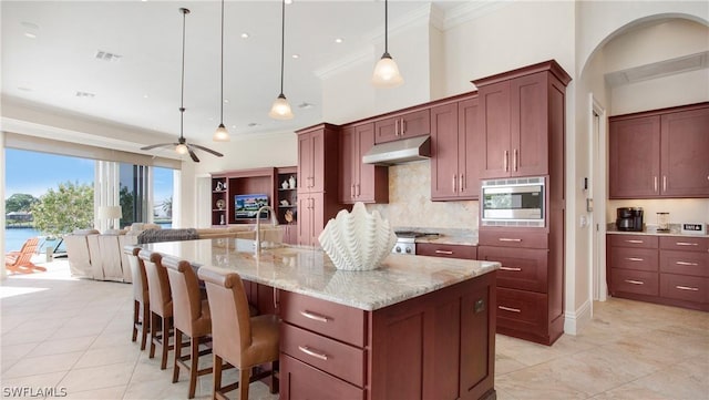 kitchen with sink, decorative light fixtures, ceiling fan, stainless steel microwave, and a kitchen island with sink