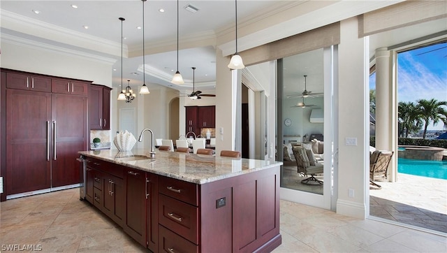 kitchen featuring sink, pendant lighting, light stone countertops, and a center island with sink