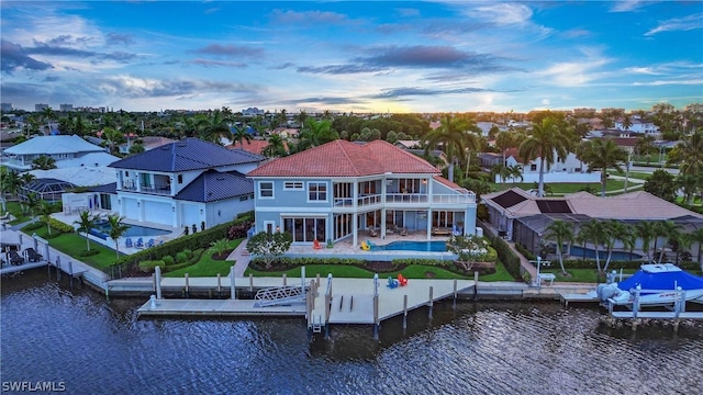 back house at dusk with a balcony, a patio area, and a water view