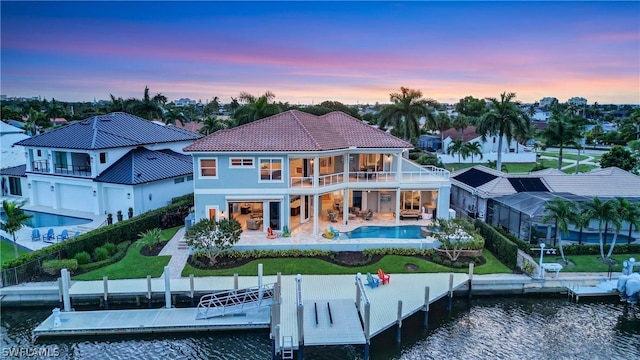 back house at dusk featuring a balcony, a water view, and a patio area