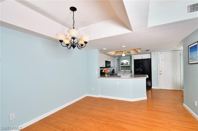 kitchen featuring kitchen peninsula, white cabinets, pendant lighting, light hardwood / wood-style floors, and black appliances