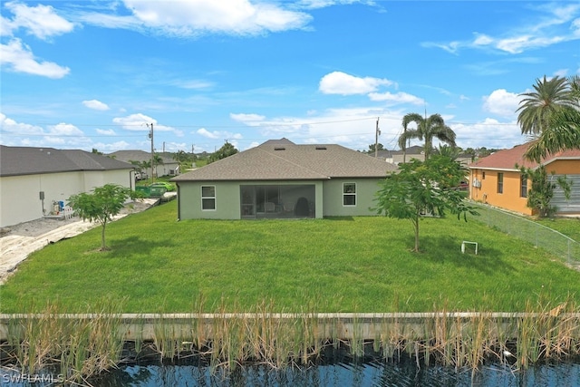 rear view of house featuring a lawn, a water view, and stucco siding