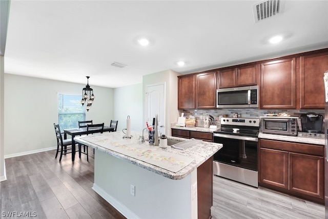 kitchen featuring stainless steel appliances, an island with sink, light hardwood / wood-style flooring, and pendant lighting