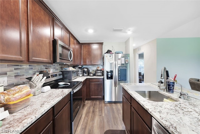 kitchen featuring light hardwood / wood-style flooring, backsplash, light stone counters, stainless steel appliances, and sink