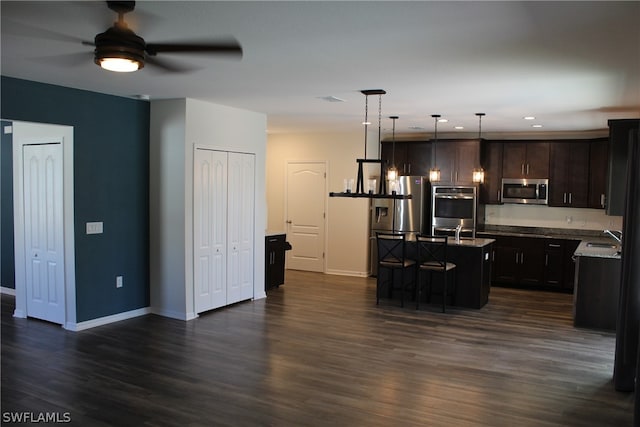 kitchen featuring dark hardwood / wood-style flooring, a kitchen island with sink, ceiling fan, stainless steel appliances, and hanging light fixtures