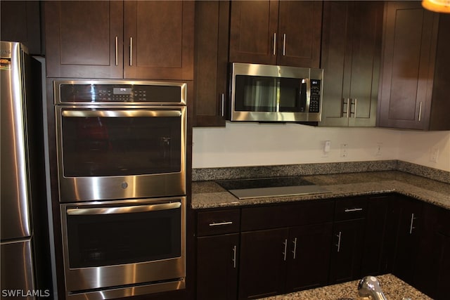 kitchen with appliances with stainless steel finishes, dark stone counters, and dark brown cabinets