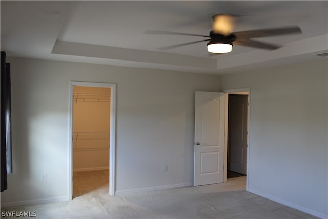 unfurnished bedroom featuring ceiling fan, a tray ceiling, a spacious closet, light carpet, and a closet