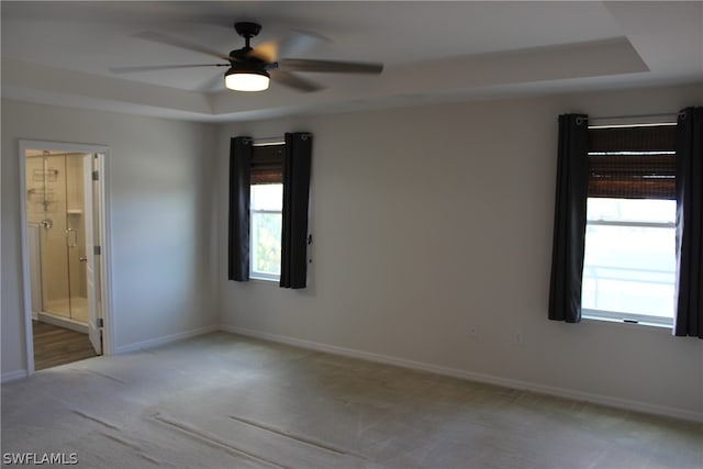 carpeted empty room featuring a wealth of natural light, ceiling fan, and a tray ceiling