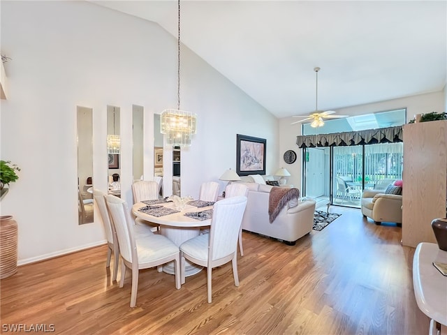 dining room with high vaulted ceiling, ceiling fan with notable chandelier, and light hardwood / wood-style flooring