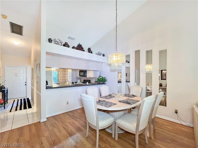 dining area featuring light wood-type flooring, an inviting chandelier, and high vaulted ceiling