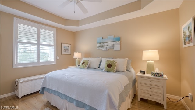 bedroom featuring a raised ceiling, ceiling fan, and light wood-type flooring