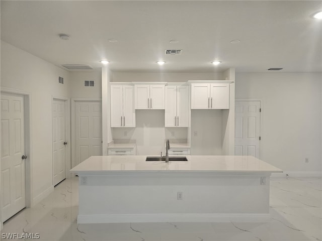 kitchen with marble finish floor, visible vents, a kitchen island with sink, a sink, and white cabinets